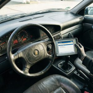 Hand hält ein Diagnosegerät mit 156.000 km neben einen Autotacho mit 82.400 km vor ein abgegriffenes Lederlenkrad.