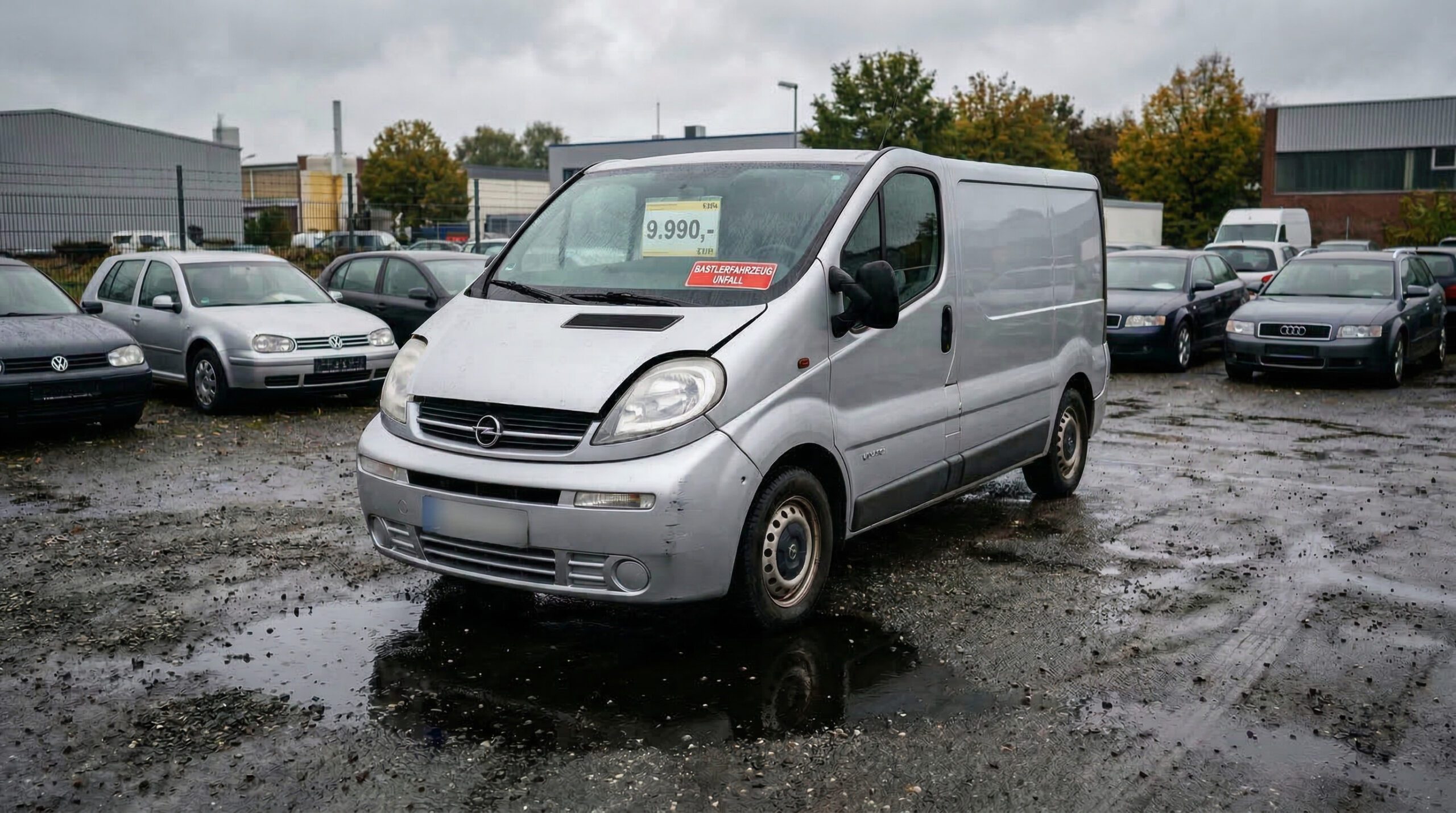 Glänzender Familien-Van auf nasskaltem Autohof mit großer schwarzer Öllache und Bastlerfahrzeug-Schild hinter der Scheibe.